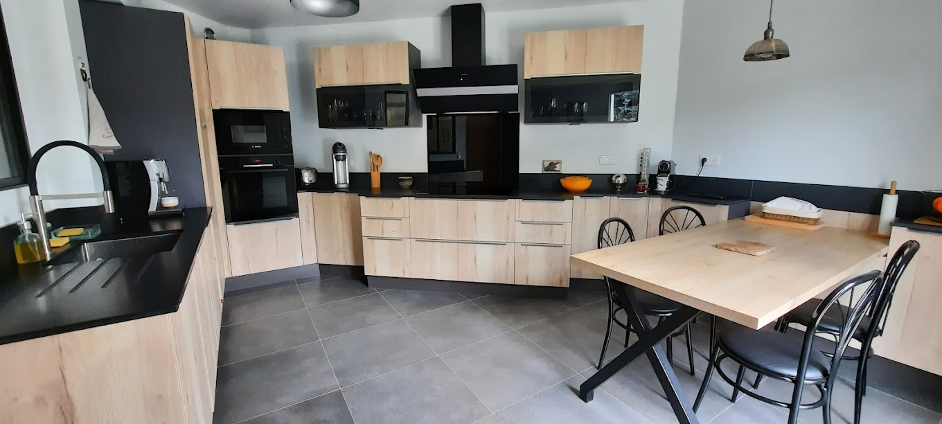 Cuisine scandinave en bois clair, plan de travail noir, îlot-table intégré
